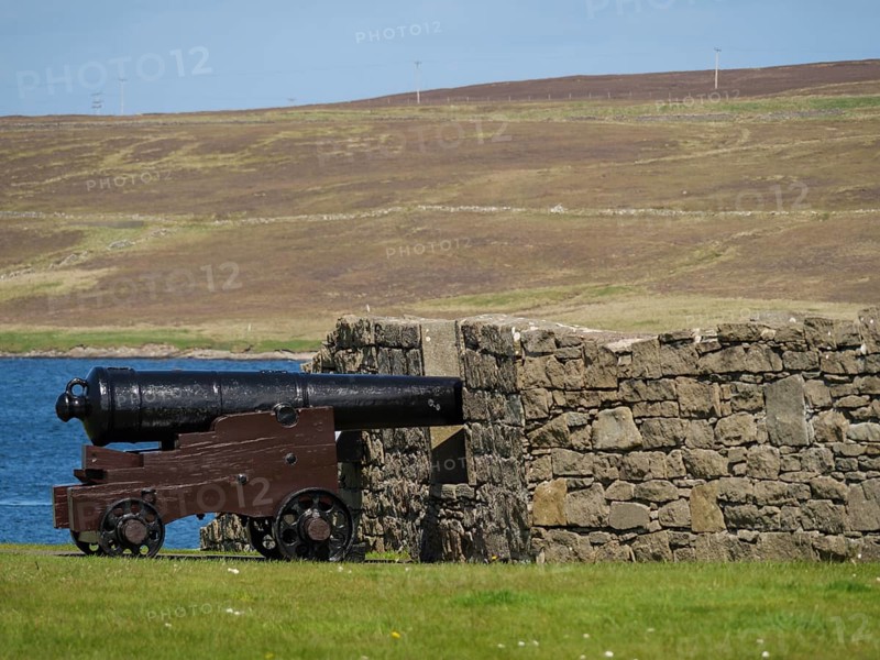 Old cannon in front of a stone wall with sea view and hills in the background, old cannon on a stone wall by the sea against a blue sky, lerwick, Scotland, United Kingdom, Europe