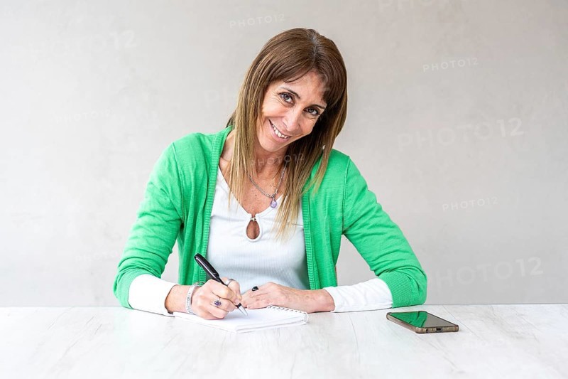 Portrait of a smiling mid-adult woman looking at the camera while she writes