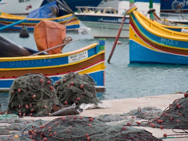 Fishing boats and nets are spread out on a pier in the harbour, many colourful fishing boats in a harbour in the Mediterranean, Marsaxlokk, malta