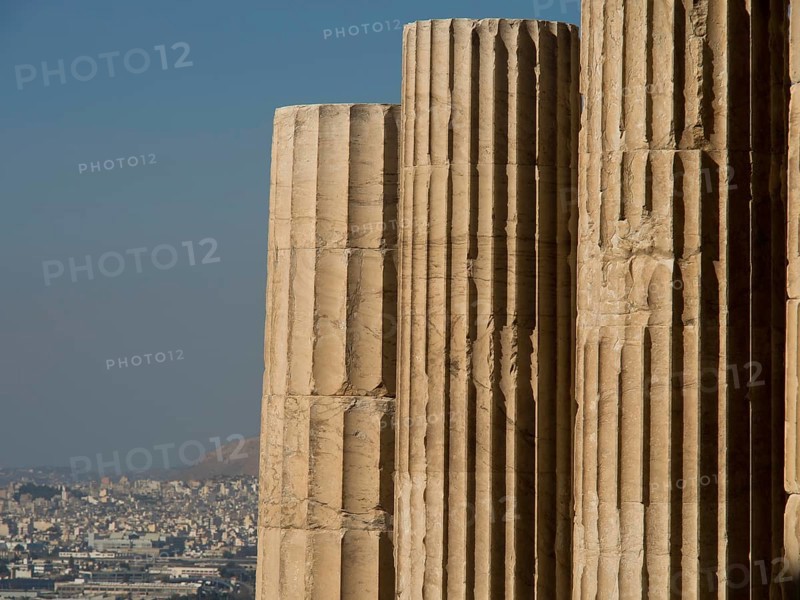 Close-up of ancient marble columns in front of a cityscape with clear sky, historical columns and ruins at an ancient site against a blue sky, Athens, Greece, Europe