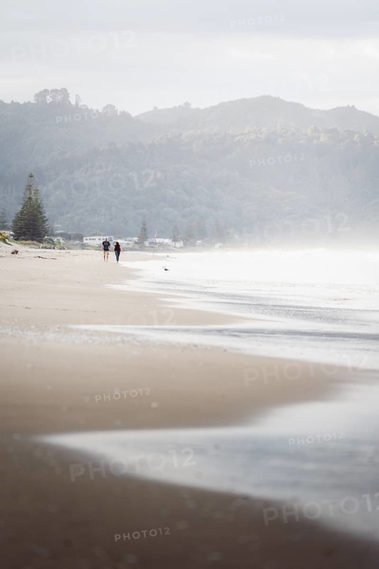 Walk on the beach at sunset, restless sea lapping waves on the beach, rocky landscape in the background. Taken at Waihi Beach in New Zealand