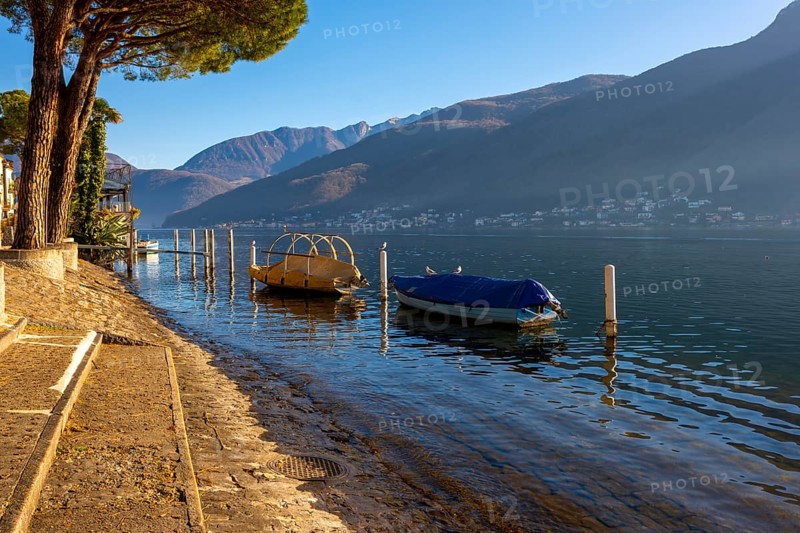 Old Beautiful Town with Trees on the Waterfront on Lake Lugano with Boat in a Sunny Day with Mountain in Morcote, Ticino, Switzerland, Europe