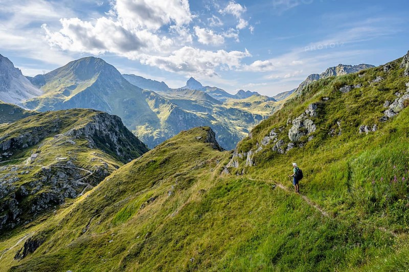 Mountaineer on a hiking trail on a grassy mountain ridge, idyllic mountain landscape with green mountain meadows, descent from Baerenbadegg, Carnic High Trail, Carnic Main Ridge, Carnic Alps, Carinthia, Austria, Europe