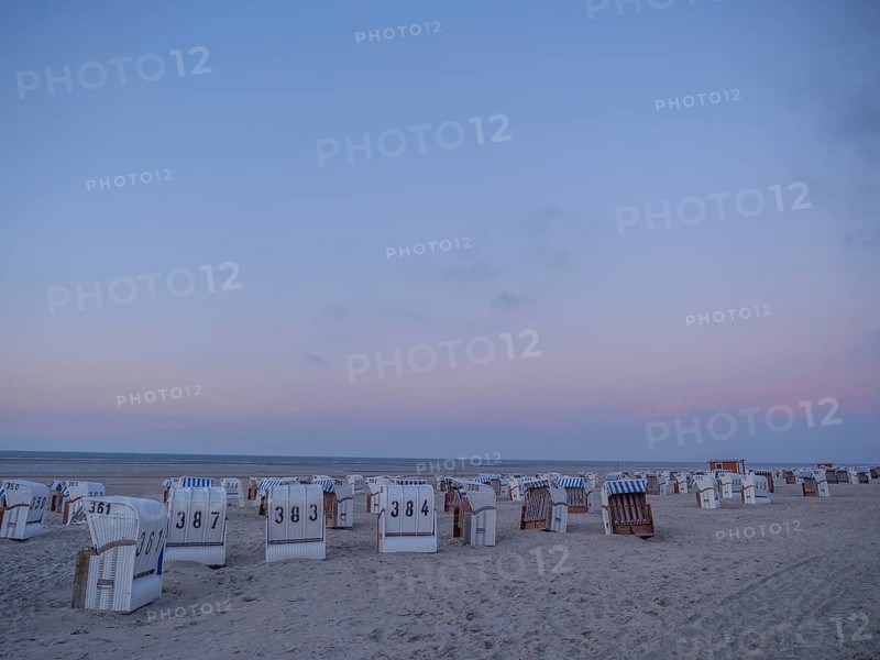 A quiet beach with white and striped beach chairs at dusk under a pastel-coloured sky, setting sun on a beach with beach chairs and clouds in the sky, spiekeroog, germany