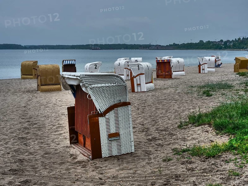 On the beach there are several beach chairs in different colours in front of a calm sea under a cloudy sky, beach chairs on a quiet sandy beach by the sea, clouds over the sea, Eckernfoerde, germany