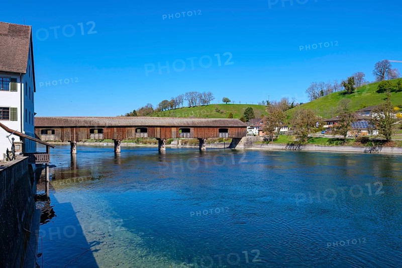 Wooden bridge over a river with old buildings in the background and a green meadow under a bright blue sky, Diessenhofen, Thurgau, Switzerland, Europe