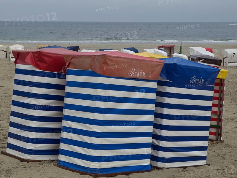 Several colourful beach chairs with stripe pattern standing on the beach in front of a cloudy sky, beach chairs and beach tents by the sea under a cloudy sky, boardwalk in the sand, Borkum, germany