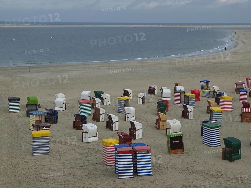 A multitude of colourful beach chairs on the extensive beach with the sea in the background, beach chairs and beach tents by the sea under a cloudy sky, boardwalk in the sand, Borkum, germany