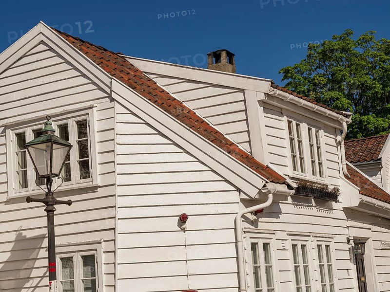 A white wooden house next to a street lamp and a green tree under a blue sky, white wooden houses with green trees and flowers against a blue sky, Stavanger, Norway, Europe