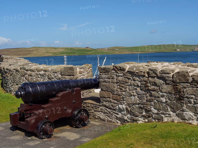 Old cannon standing in front of a stone wall with sea view and green hills under blue sky, old cannon on a stone wall by the sea in front of blue sky, lerwick, Scotland, United Kingdom, Europe