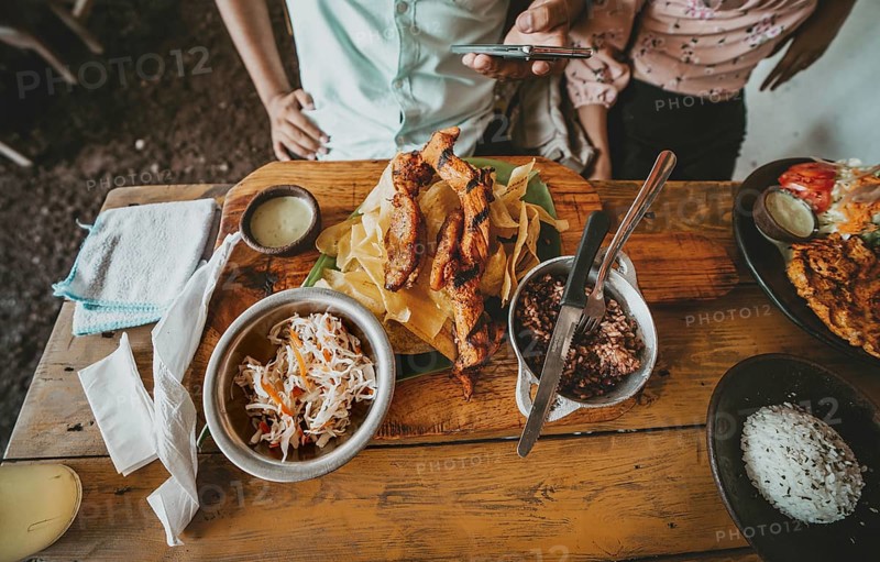 Person eating a traditional roast beef with slices of banana and gallopinto served on a wooden table. Close up of traditional roast meats and gallopinto