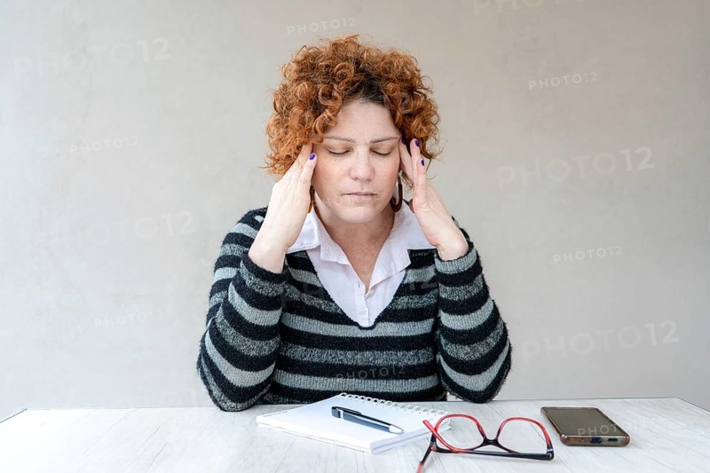A mid-adult redhead woman with a headache is rubbing her temples