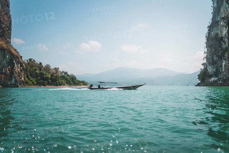 Boat glides on clear water near majestic rock formations. Khao Sok National Park, Thailand, Asia