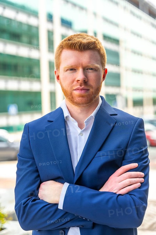 Vertical portrait of a confident young businessman looking at camera standing with arms crossed outdoors