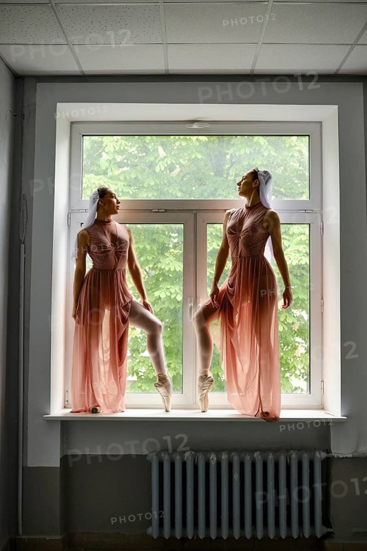 Two graceful ballerinas in transparent long dresses stand on the windowsill in the corridor