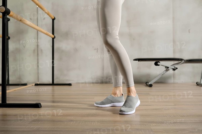 Slender female legs in sports leggings and sneakers near the handrail in the gym