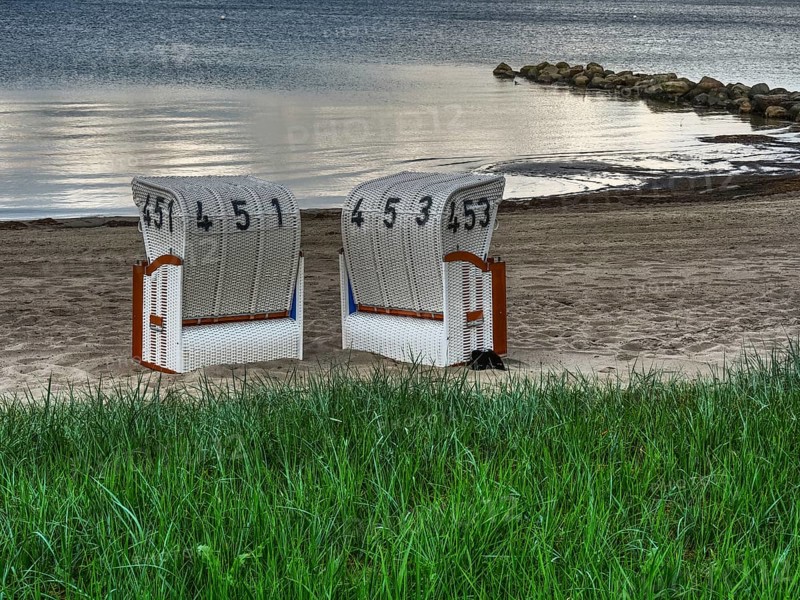 Two white beach chairs in front of a green meadow, sandy beach and calm sea in the background, beach chairs on a quiet sandy beach by the sea, clouds over the sea, Eckernfoerde, germany