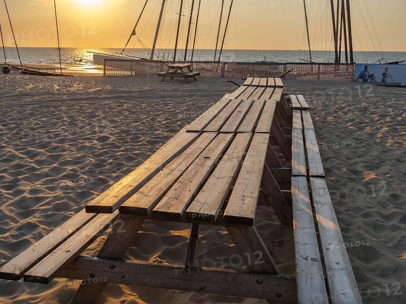 Long picnic tables on sandy beach at sunset, boats in the background, warm and relaxing atmosphere, sunset at the sea with boats and a bench, sand on the beach, de Haan, Belgium, Europe