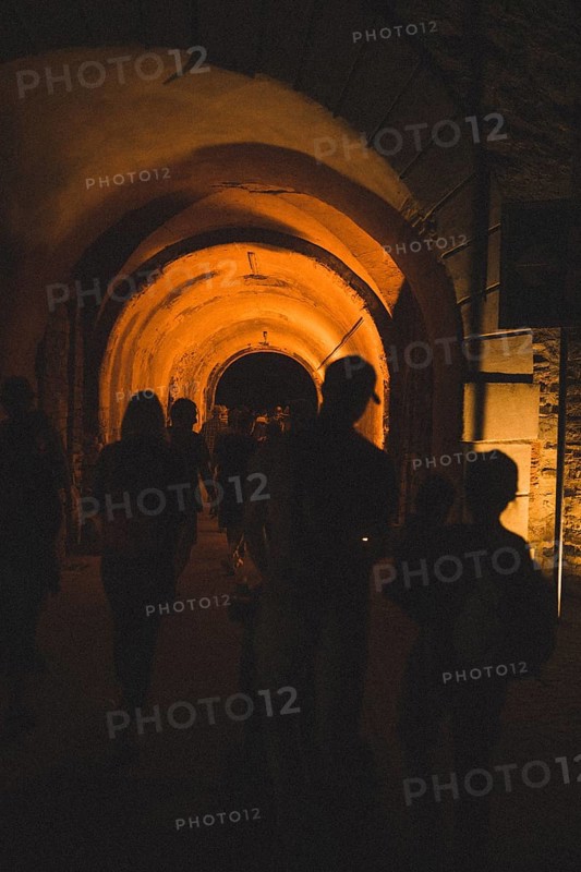 Silhouettes of people walk through a tunnel with warm lights. Ehrenbreitstein Fortress, Koblenz Germany