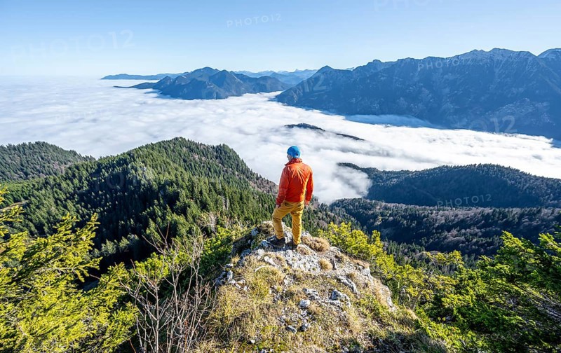 Mountaineer on the rocky summit of the Ettaler Manndl, view over mountain landscape and sea of clouds, high fog in the valley, Ammergau Alps, Bavaria, Germany, Europe