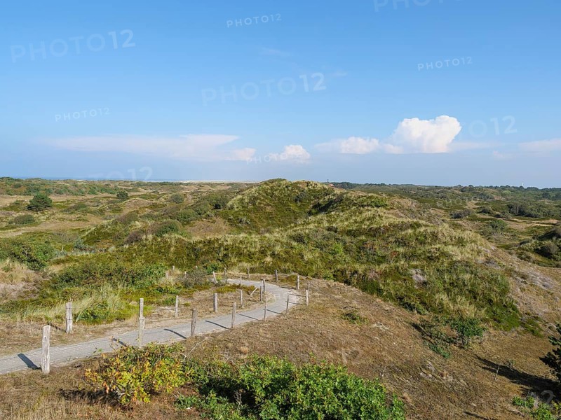 Hilly landscape with a hiking trail surrounded by grass and bushes under a blue sky with clouds, dunes and beach at the sea with dune grass and beach chairs in front of a blue sky, Spiekeroog, Germany, Europe