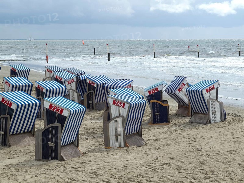 Several blue and white beach chairs stand on a sandy beach with a cloudy sky and the sea in the background, blue and white striped beach chairs on the seashore, Norderney, Germany, Europe