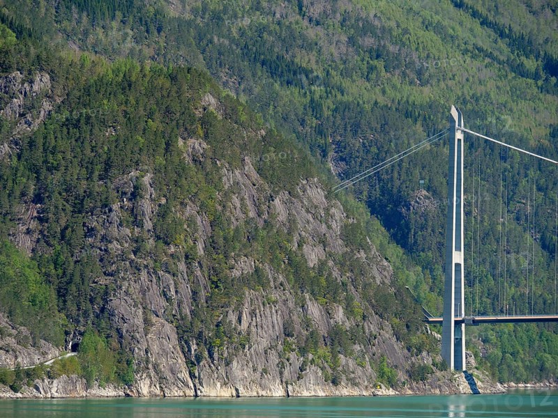 High bridge over turquoise water, surrounded by forested mountains and rocky cliffs, bridge in a fjord with snow-capped mountains and green trees, greenish shimmering water, eidfjord, Norway, Europe