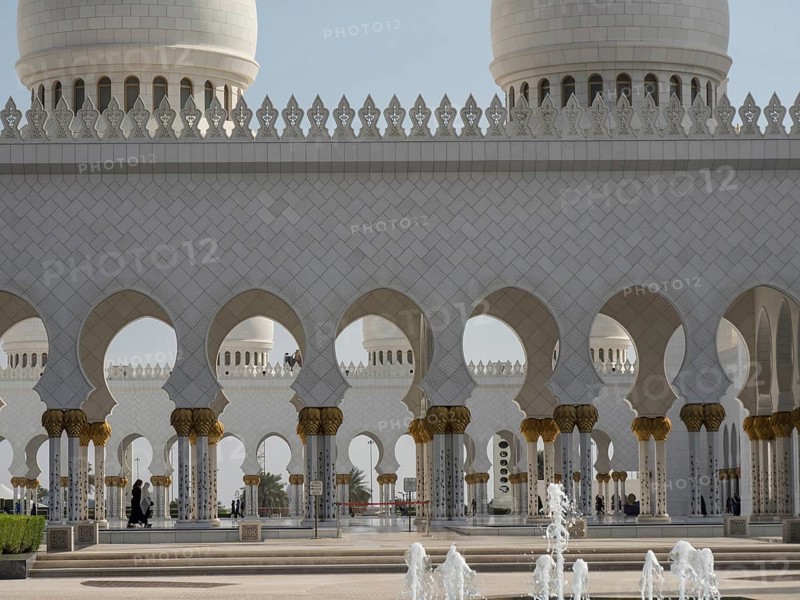 Mosque with arches and ornately decorated columns under a clear sky and visible fountains, beautiful mosque with white domes and beautiful minarets, abu dhabi, arab emirates
