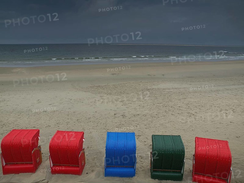 Five colourful beach chairs in red, blue and green stand on a quiet beach in front of a cloudy sky, beach chairs and beach tents by the sea under a cloudy sky, boardwalk in the sand, Borkum, germany