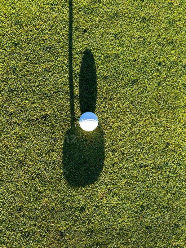 Golf Ball on Putting Green with Shadow and Shadow of a Golf Club Putter in a Sunny Day in Switzerland