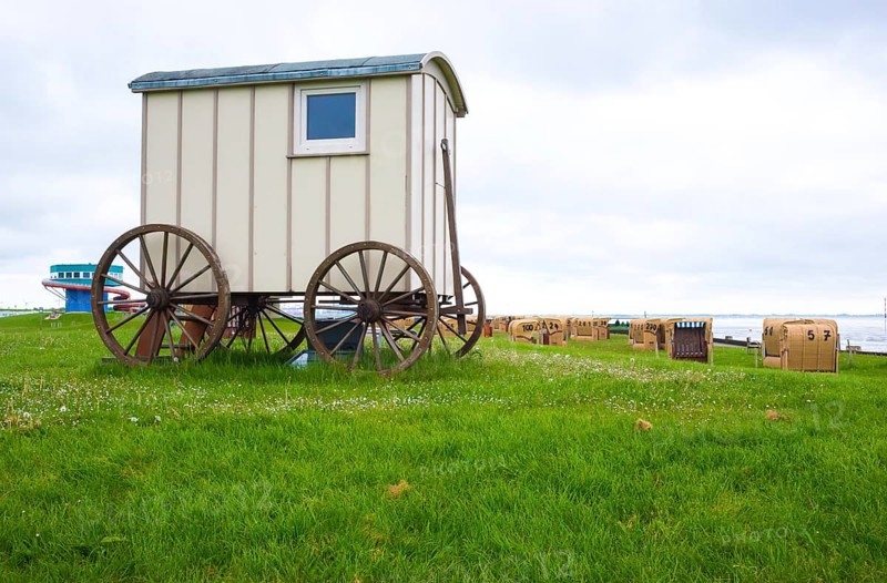 Old wooden cart, bathing cart with drawbar and large wooden wheels on a green meadow, in the background many beach chairs, cloudy day, deserted, sea at low tide, low tide, North Sea, North Sea resort Wremen, Lower Saxony Wadden Sea National Park, World Heritage Site, Wurster North Sea coast, Land Wursten, district of Cuxhaven, Lower Saxony, Germany, Europe