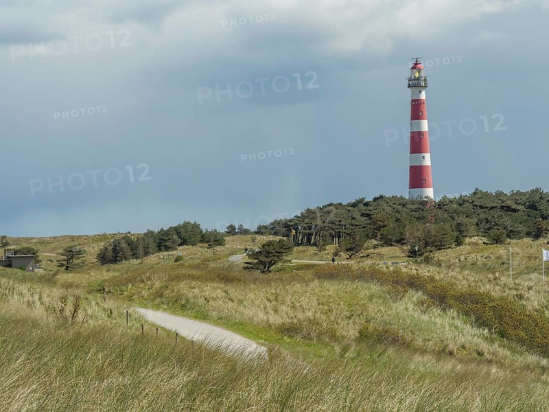A red and white striped lighthouse in a grassy and wooded dune landscape under a cloudy sky, red and white lighthouse in the dunes, nes, ameland, the netherlands