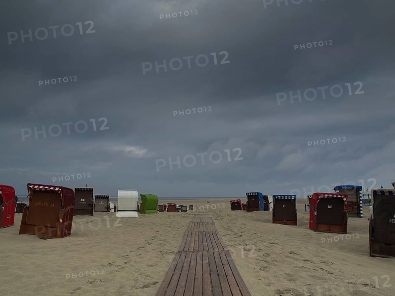 Dark clouds hanging over a beach with scattered beach chairs and a wooden jetty, beach chairs and beach tents by the sea under a cloudy sky, boardwalk in the sand, Borkum, Germany, Europe