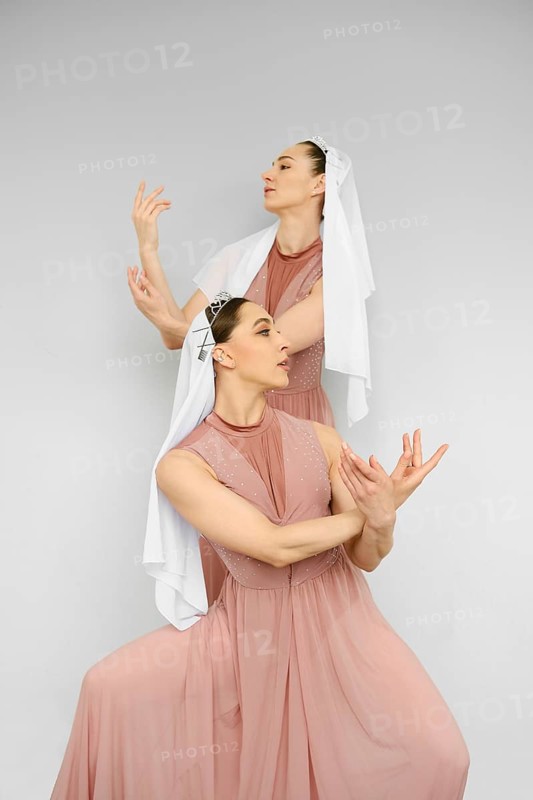 Two female dancers perform hand movements on grey background