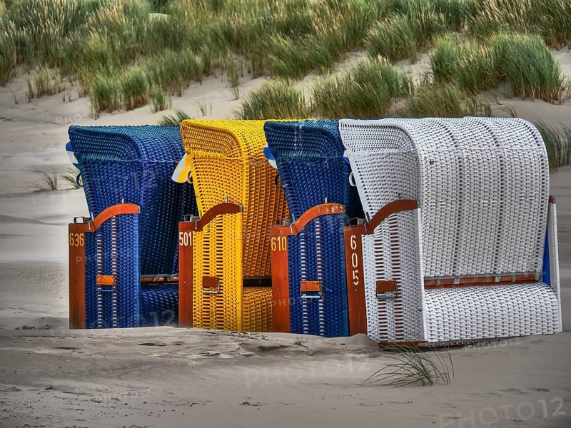 Close-up of colourful beach chairs made of rattan in blue, yellow and white in a dune landscape, colourful beach chairs on the beach and in the dunes under an overcast sky by the sea, Juist, Germany, Europe