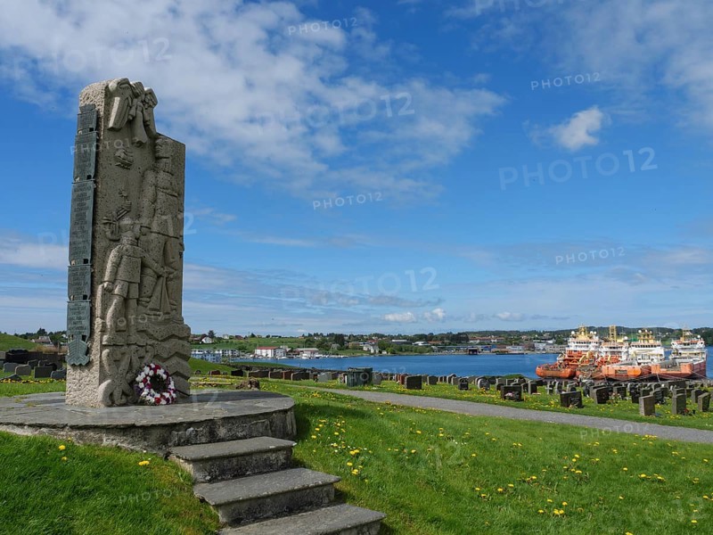 Stone memorial on a cemetery with a beautiful view of the water and the neighbouring boats, old stone church and many gravestones on the water with ships in the background, haugesund, norway