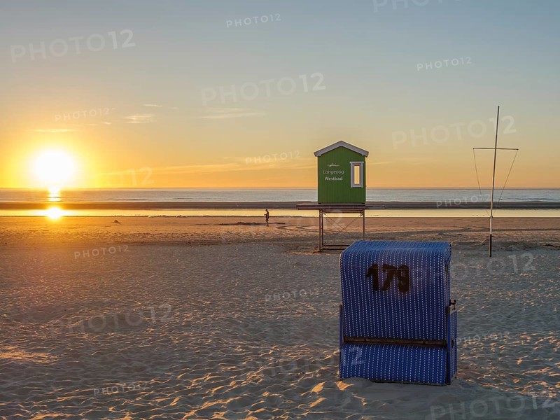 Sunset on the beach with a blue beach chair and a lifeguard house in the distance, beautiful sunset on the beach of an island with beach chairs in the foreground and the calm sea in the background, langeoog, germany