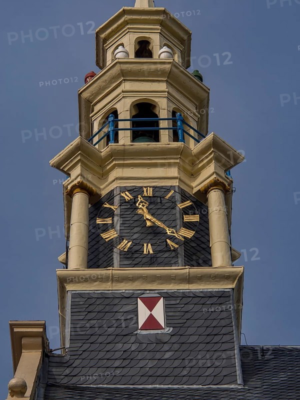 Close-up of a clock on a historic clock tower with blue and yellow decoration, tower with a golden spire and a large clock against a blue sky, hoorn, the netherlands