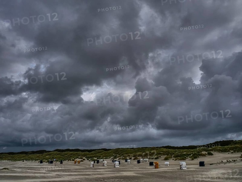 Threatening sky over an empty beach with scattered beach chairs, colourful beach chairs on the beach and in the dunes under an overcast sky by the sea, Juist, Germany, Europe