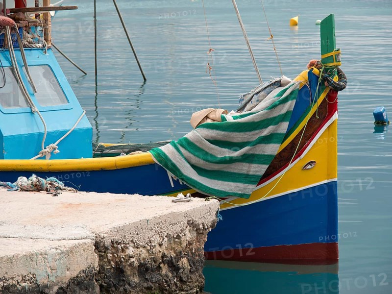 Small colourful boat moored at the pier, covered with a striped cloth, many colourful fishing boats in a harbour in the Mediterranean Sea, Marsaxlokk, malta
