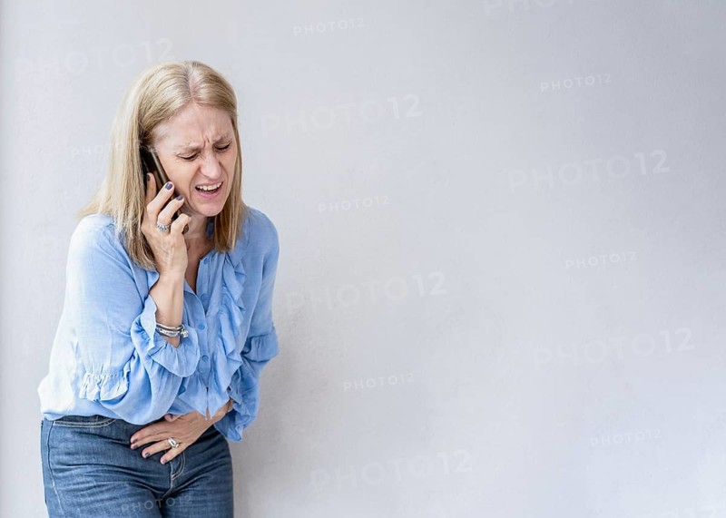 A blonde woman is calling her doctor because she is suffering an appendix pain