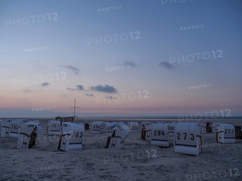 A calm dusk on a beach with white beach chairs and a soft sky, setting sun on a beach with beach chairs and clouds in the sky, spiekeroog, germany
