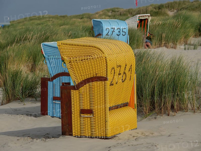 Close-up of yellow and blue beach chairs in the dunes on the beach, colourful beach chairs on the beach and in the dunes with overcast sky, red wooden boat and yellow beach chair, Juist, Germany, Europe