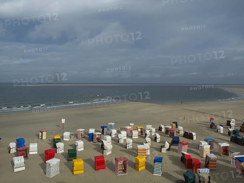 Colourful beach chairs are spread over the sandy beach, the sea and clouds can be seen in the background, beach chairs and beach tents by the sea under a cloudy sky, boardwalk in the sand, Borkum, germany