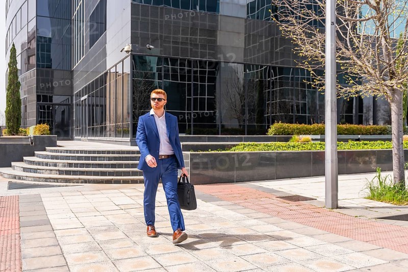 Businessman carrying laptop bag walking along city next to financial building