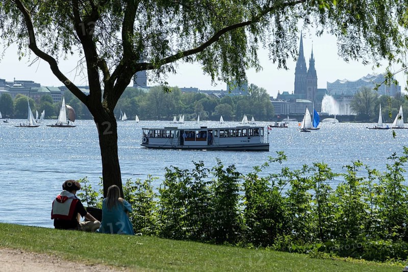 Symbolic picture weather, leisure activity, summery spring, silhouette of a couple in a park, behind them a barge, sailing boats and rowing boats against a blue sky on the Alster in Hamburg, Germany, Europe