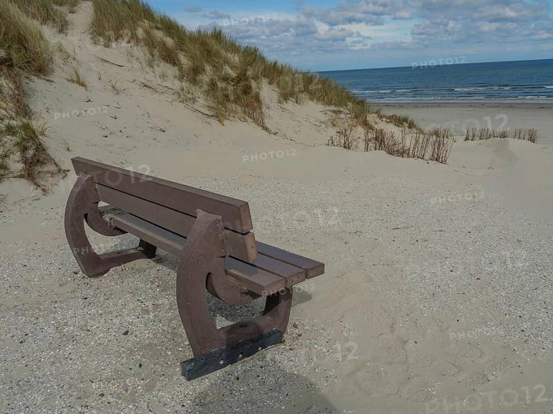 Beach scene with a wooden bench, dunes and sea under a cloudy sky, dunes on an island with a blue boat and a bench, clouds and sand by the sea, nees, ameland, the netherlands