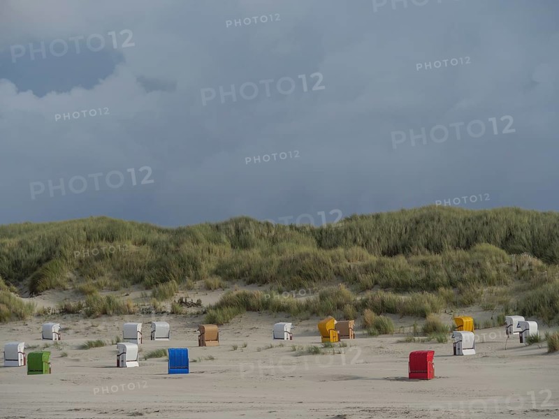 Beach chairs are spread out in front of a hilly dune landscape under a cloudy sky, colourful beach chairs on the beach and in the dunes under a cloudy sky, red wooden boat and yellow beach chair, Juist, Germany, Europe