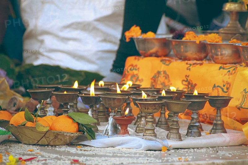 Close up to lit brass ghee lamps or butter lamps and sacred marigold flowers offering during religious sacred ritual for Tibetan Losar or New Year