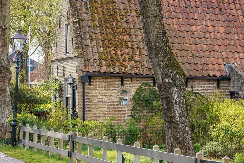 Historic house with brick wall, fence and street lamp, surrounded by trees and a garden, historic houses in a small village with small streets and trees in spring, Nes, Ameland, Netherlands